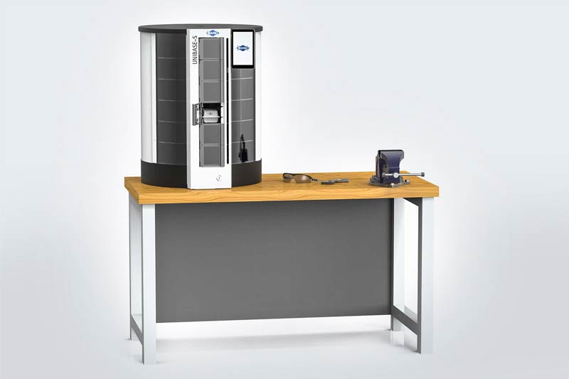 The UNIBASE-S tool dispensing system is placed on a workbench. Next to it are protective goggles and tools.