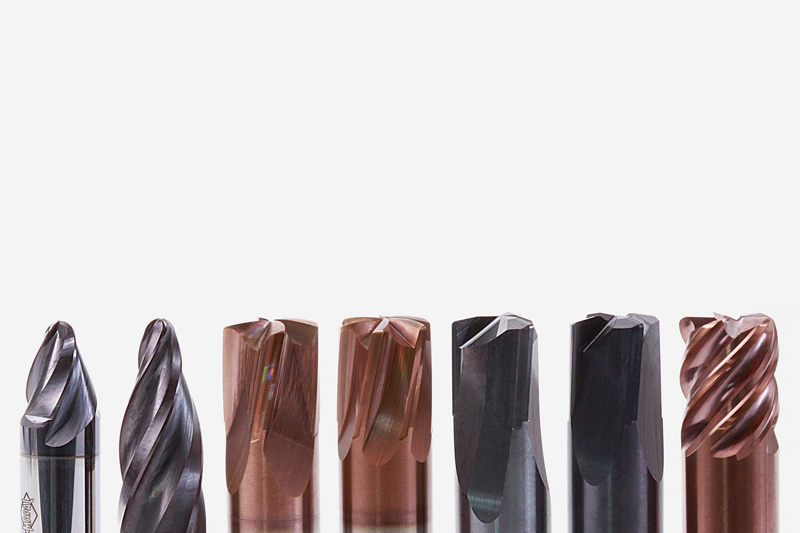 Es sind sieben Fräser aus Vollhartmetall in einer Reihe zu sehen. Sie haben unterschiedliche Formen und Beschichtungen.