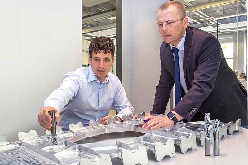 A large structural part in front of Dietmar Maichel and Axel Fleischer. Next to it are milling cutters for its machining.