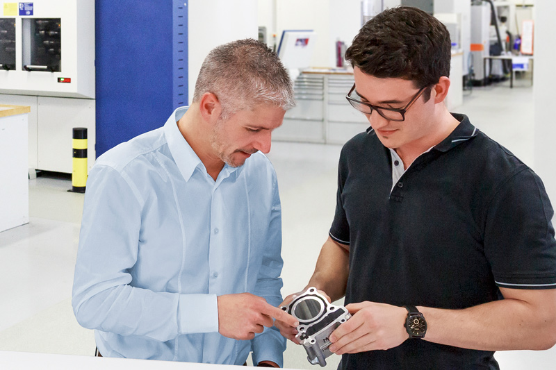 The picture shows two MAPAL employees who discuss a workpiece at the test centre in Aalen.